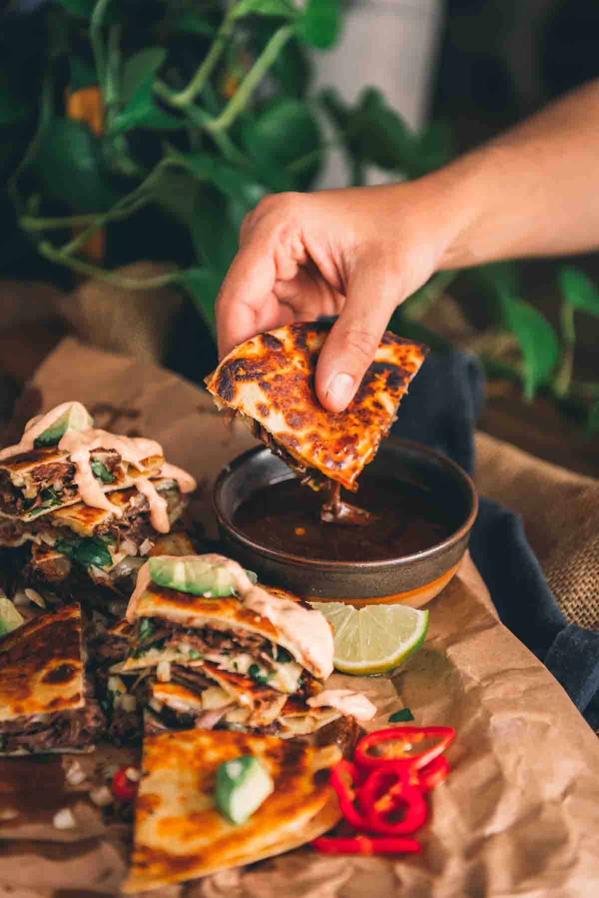 Hand dipping quesadilla wedge into the broth.