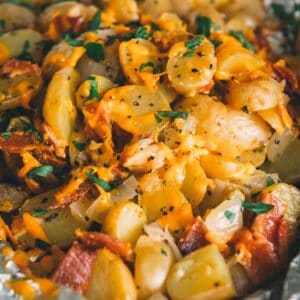 Close up of cooked potatoes, with melted cheese, bacon and herbs.