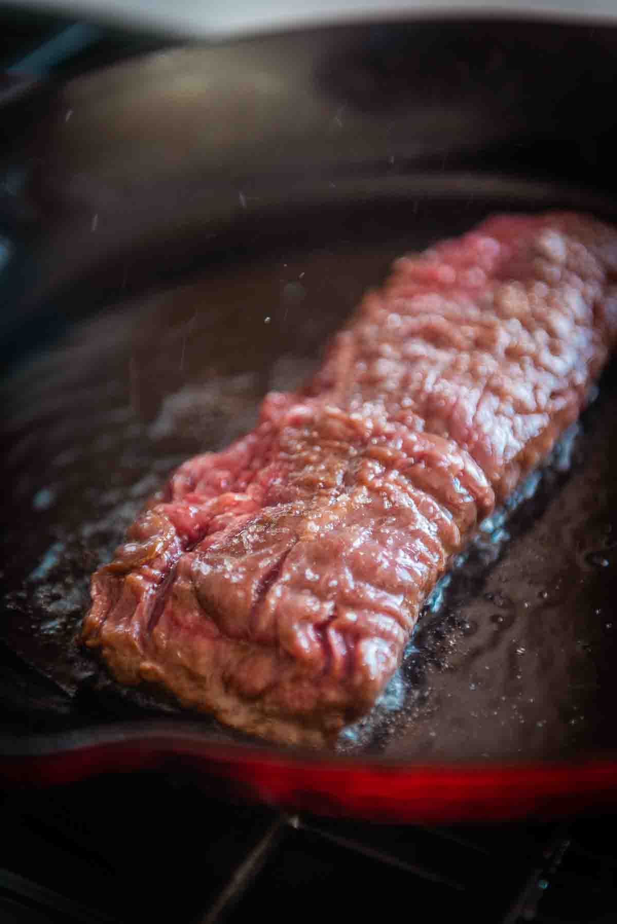 Sierra steak placed in a hot cast iron pan, close up showing the grain of the beef. 