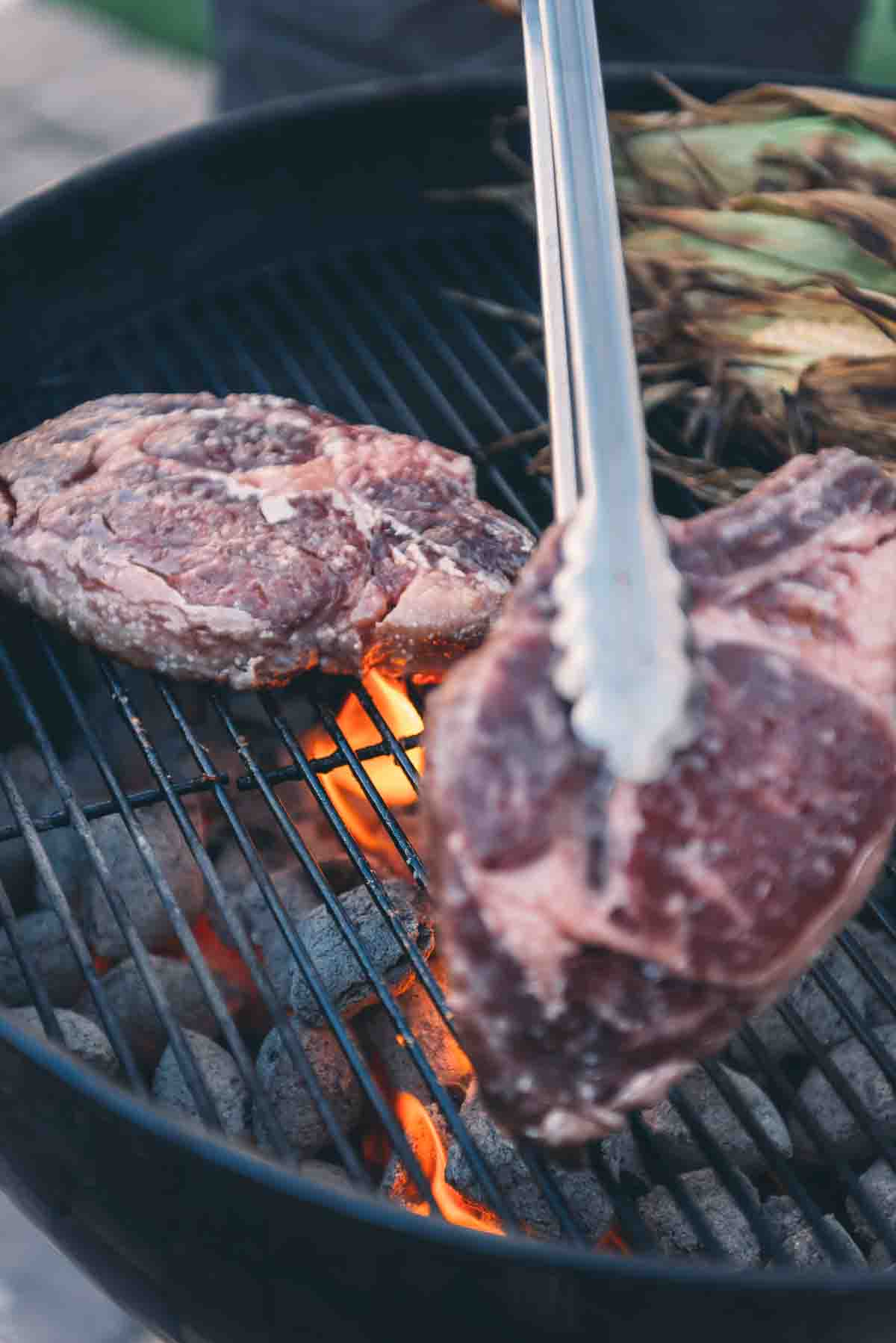 Steaks being placed over charcoal grill.