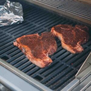 Two grilled steaks are cooking on an outdoor grill.