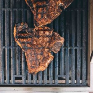 A grilled t-bone steak is being cooked on a grill.