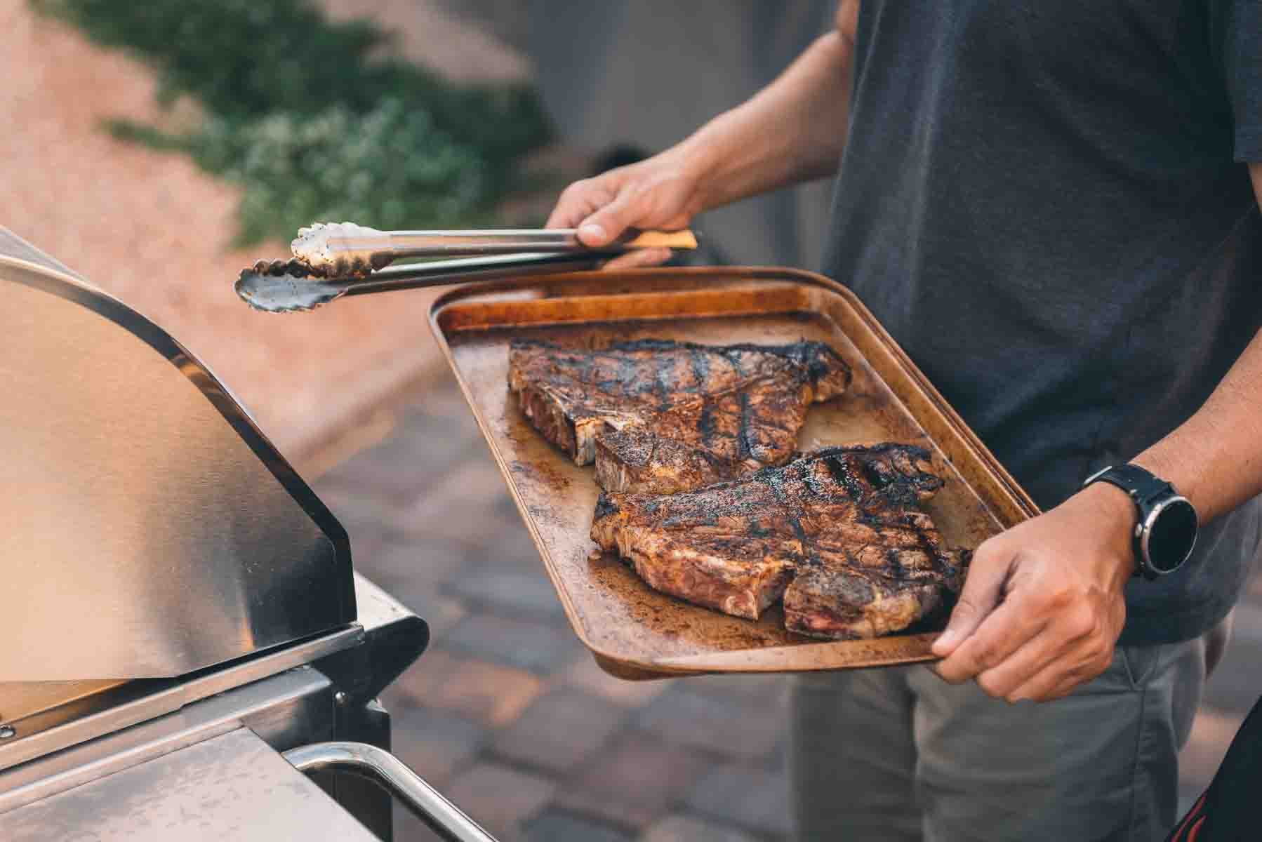 A man is grilling a t-bone steak.