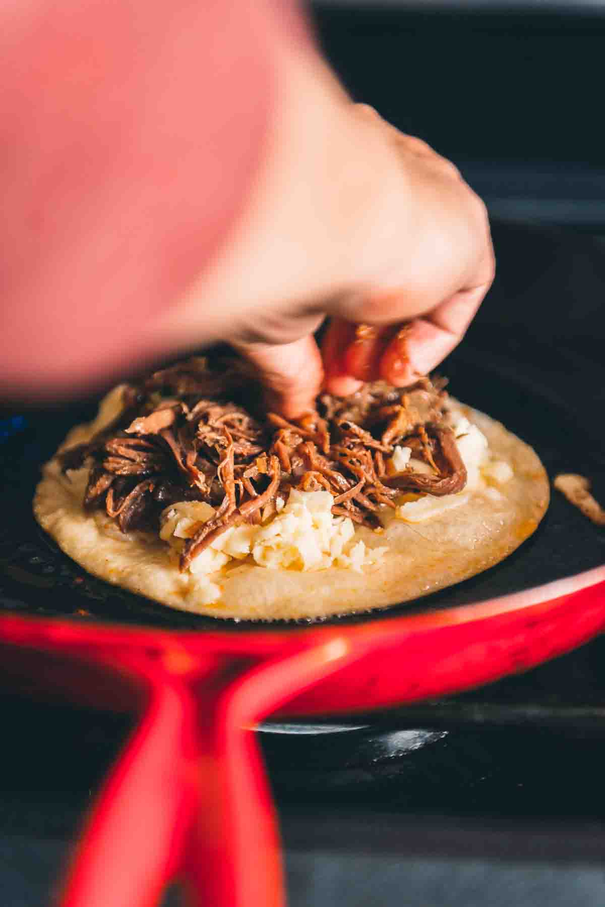 Hand placing birria meat onto the tortilla. 