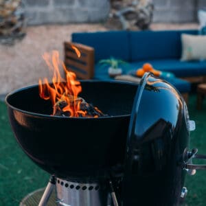 A smoky black BBQ grill with flames on it.