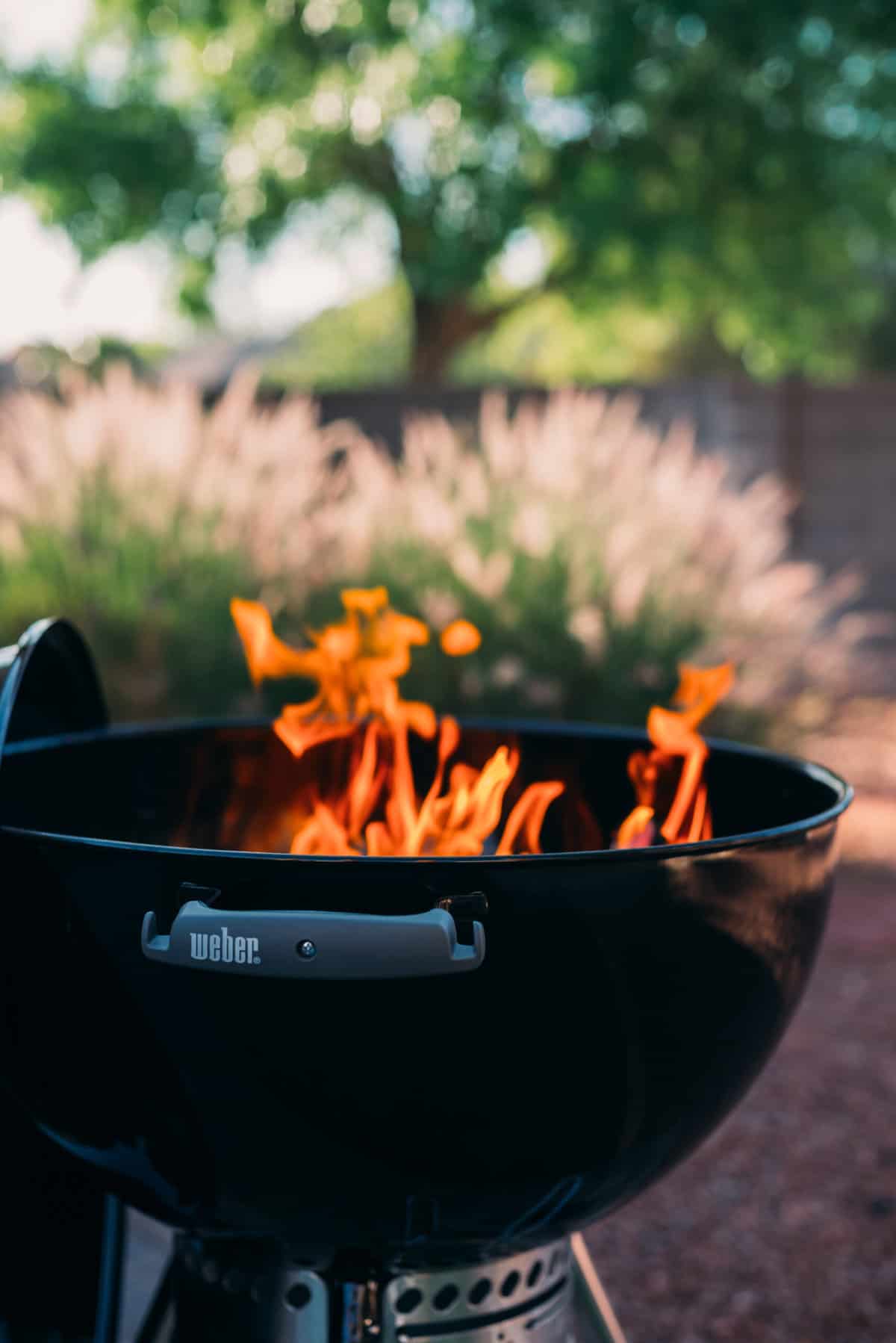 Weber kettle grill with coals lit inside waiting for the flames to die down. 