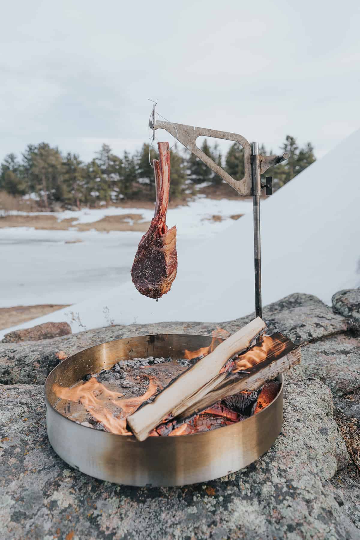 Hanging tomahawk steak over a campfire.