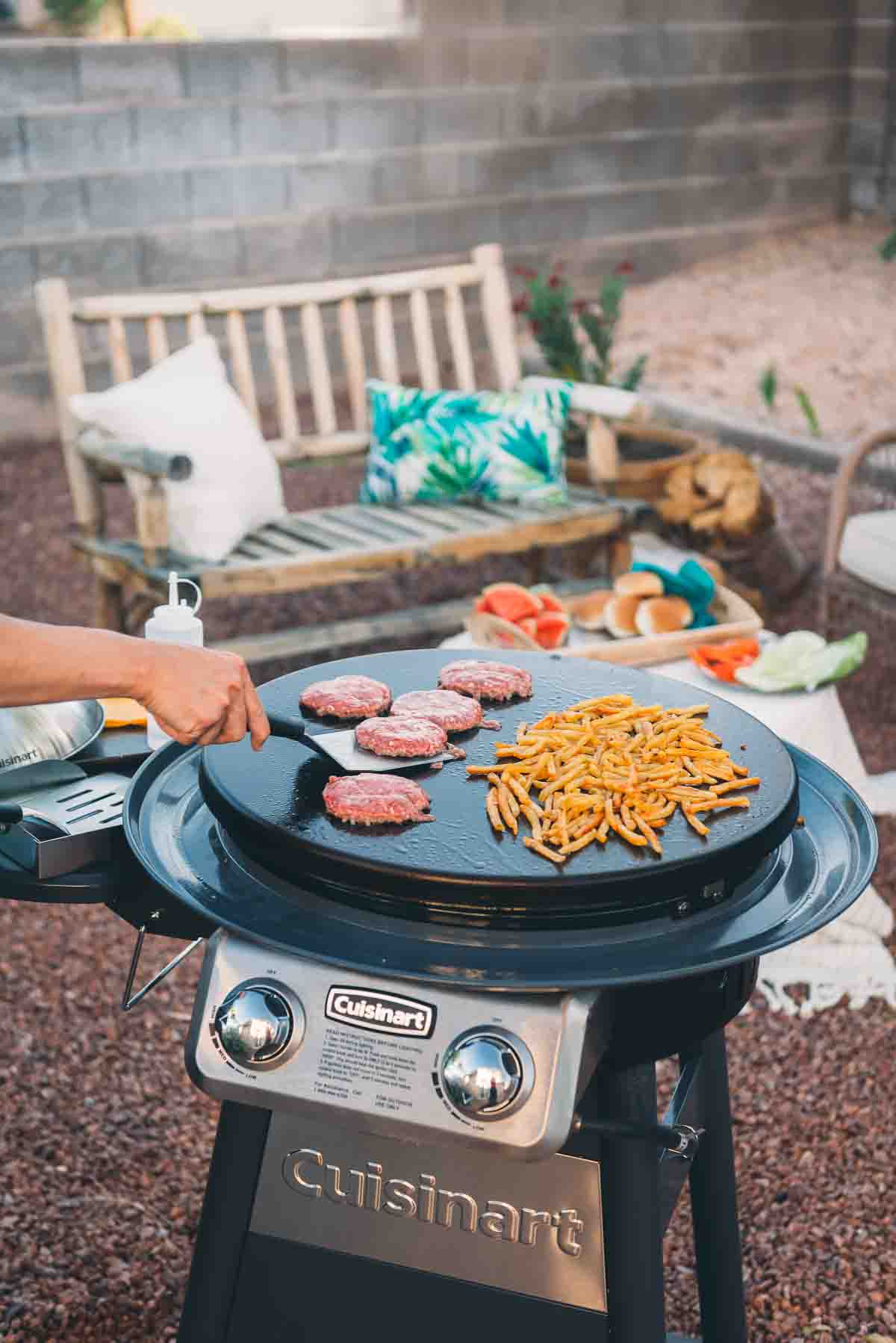 Cuisinart griddle grill with burgers and fries on the cooktop being flipped.