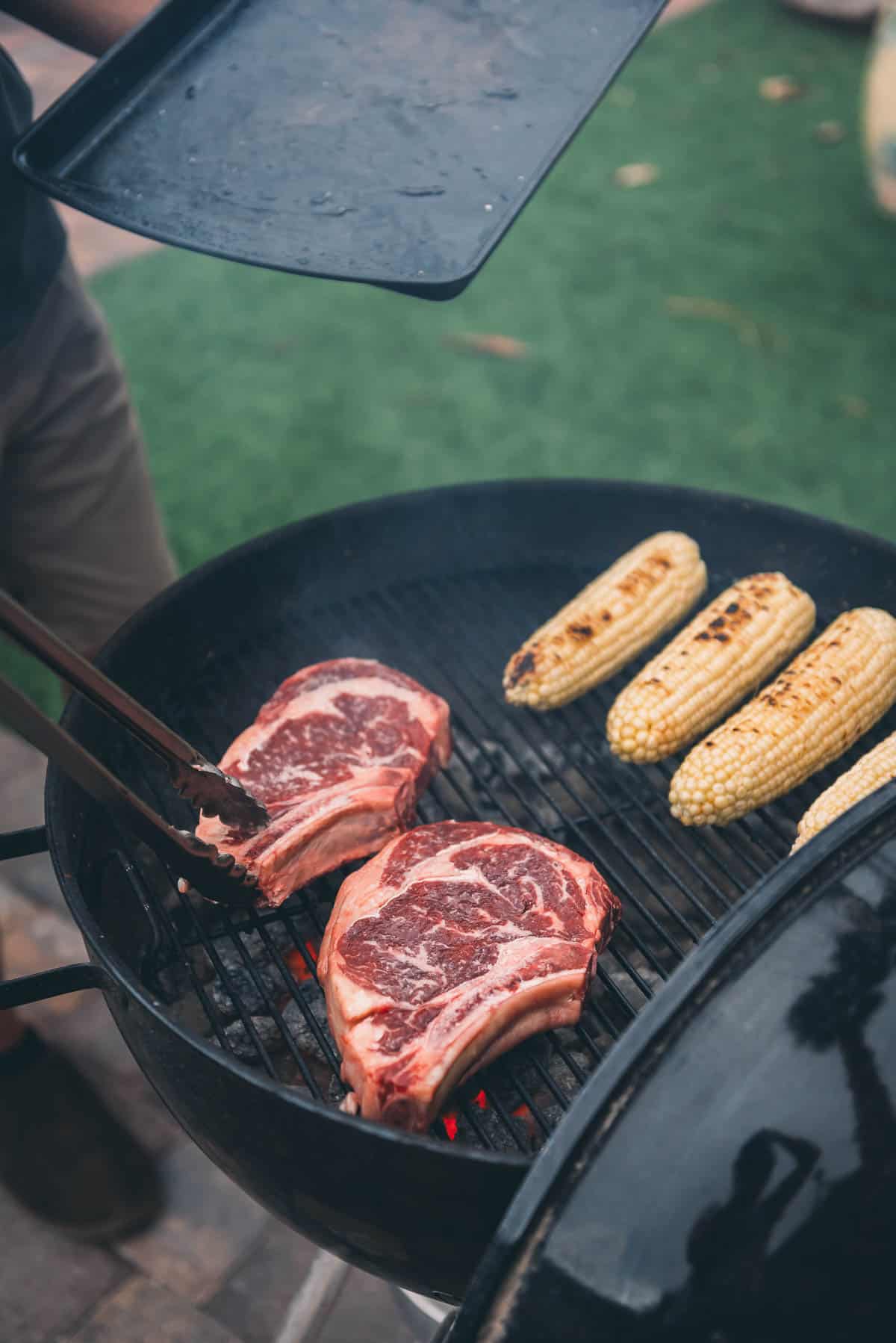 Ribeye steaks and corn on a charcoal grill. 