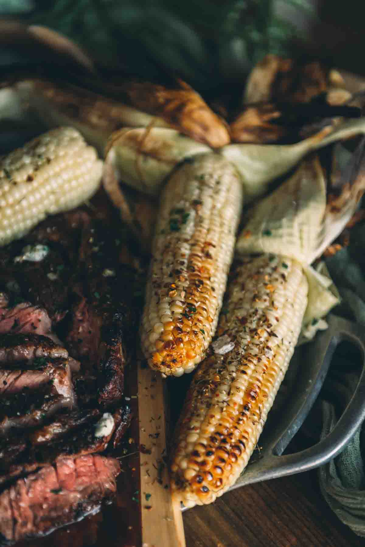 Close up of corn on the cob, with grilled charred kernels topped with spices on a serving board.