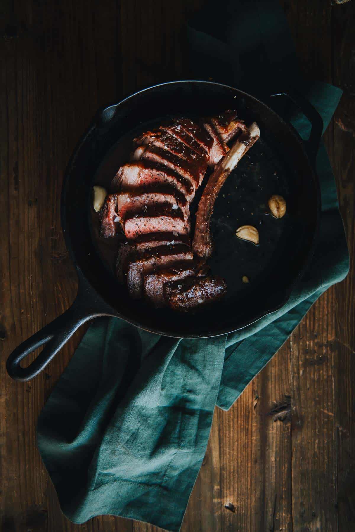 Steak carved from bone and sliced into strips, served in skillet with garlic cloves, salt and pepper sprinkled over top. 