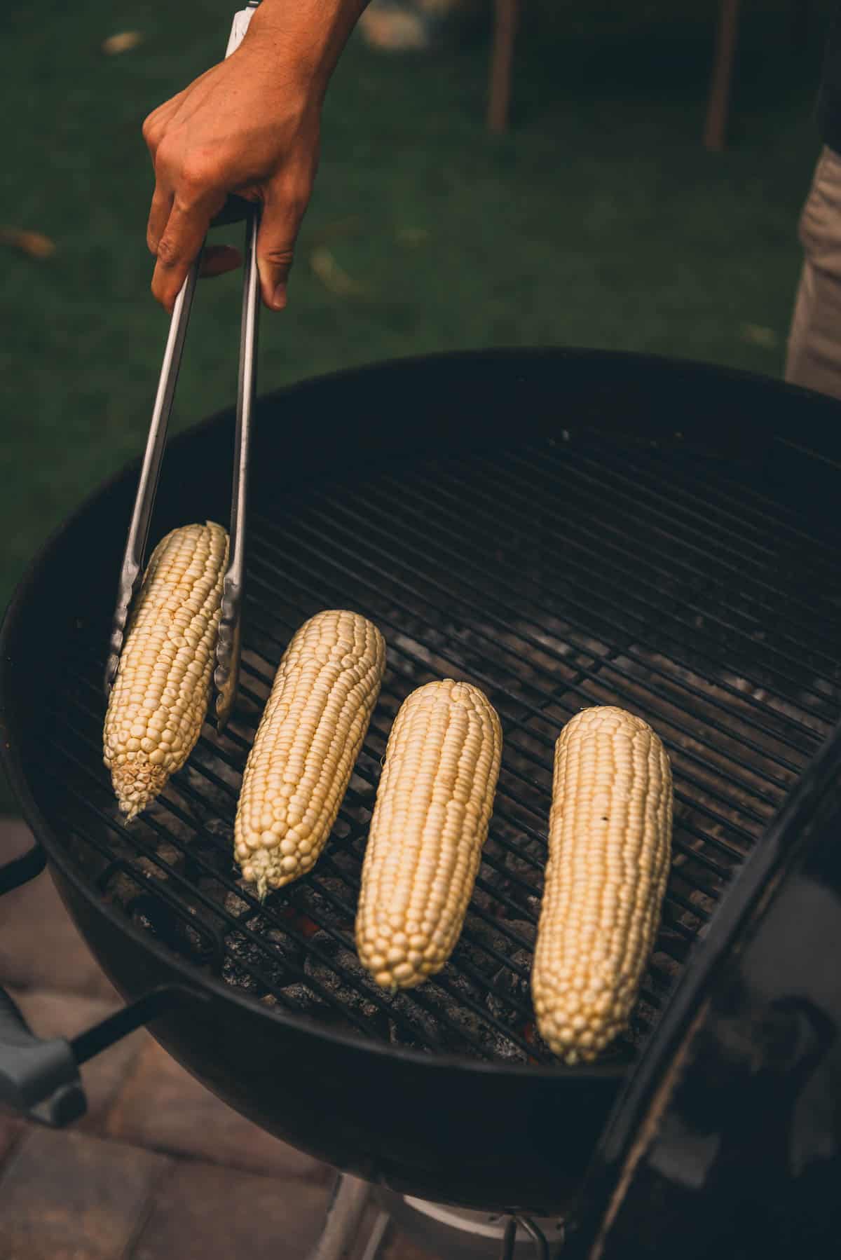 Hand with tongs placing corn on the grill.