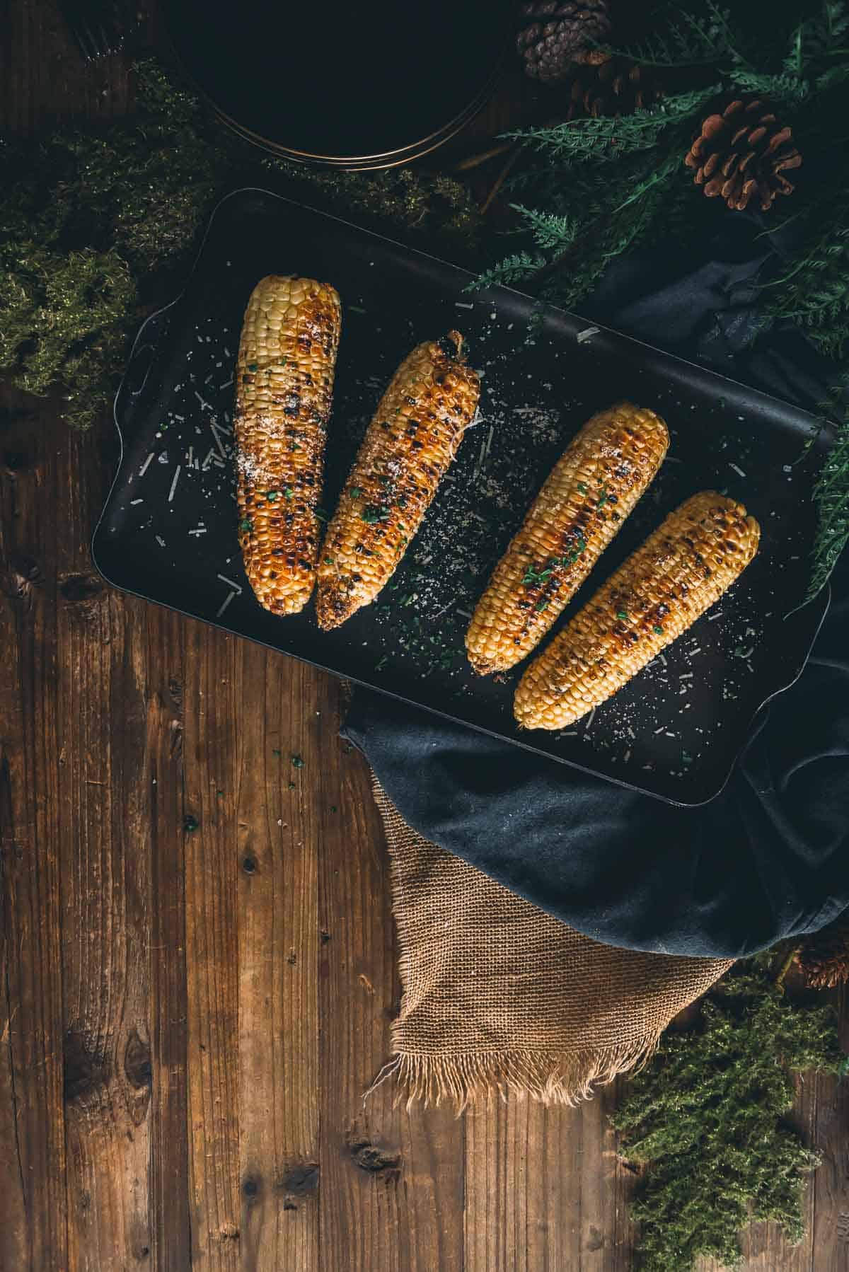 Grilled corn on the cob on a platter for serving garnished with herbs and spices. 