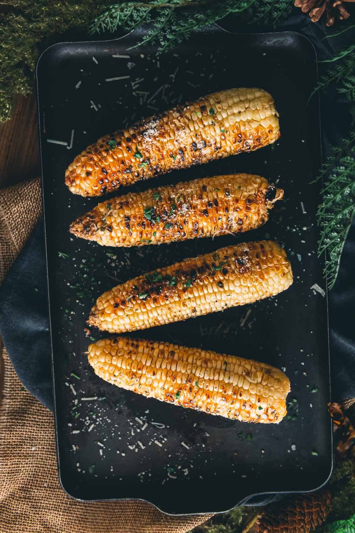 Grilled corn on a platter for serving with charred kernels and a dusting of salt, pepper, spices  and grated parmesan cheese. 
