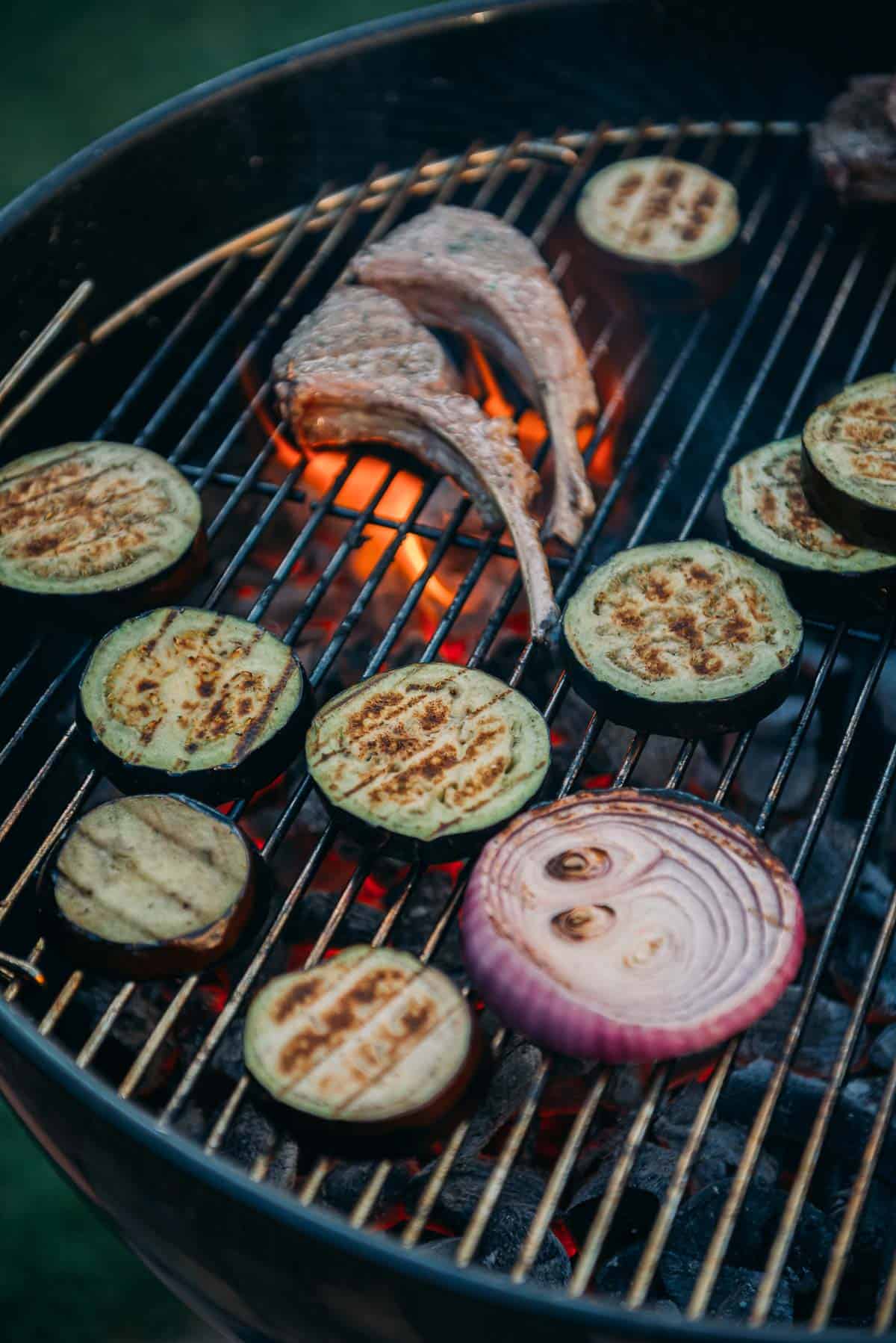 Grill grate filled with veggies and lamb chops. 