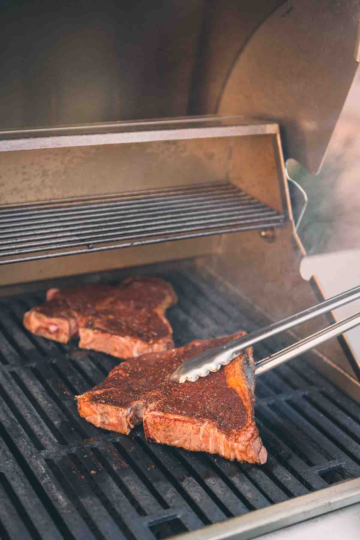 Steaks being flipped with tongs.
