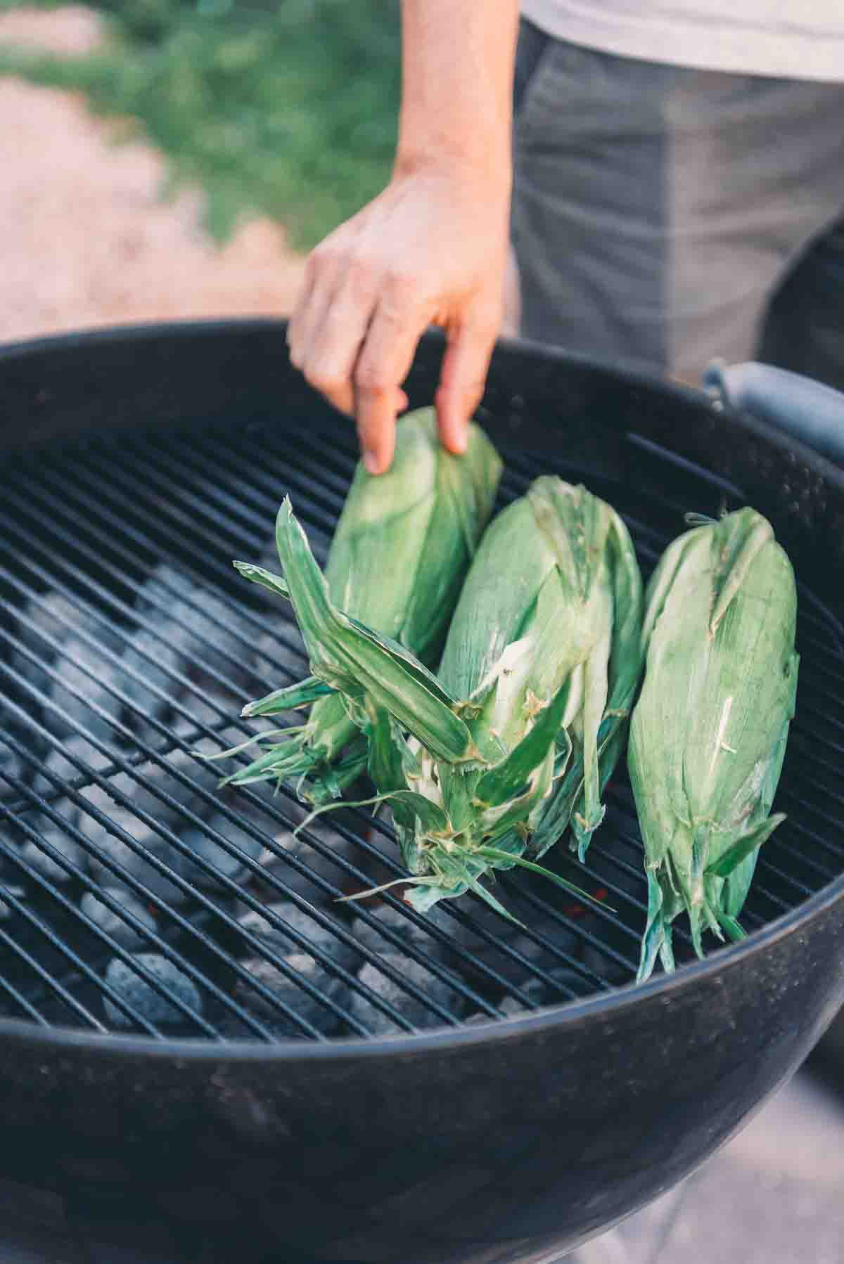 Hand placing corn on the grill. 
