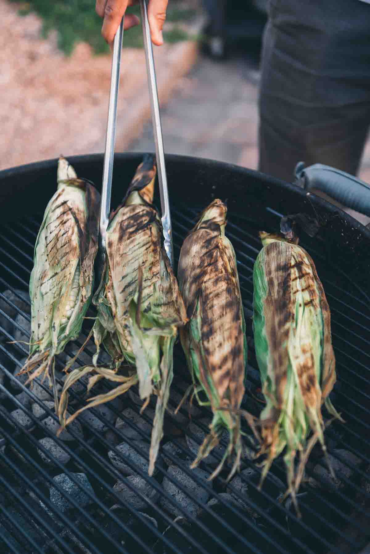 Tongs rotating corn to show charred sides. 
