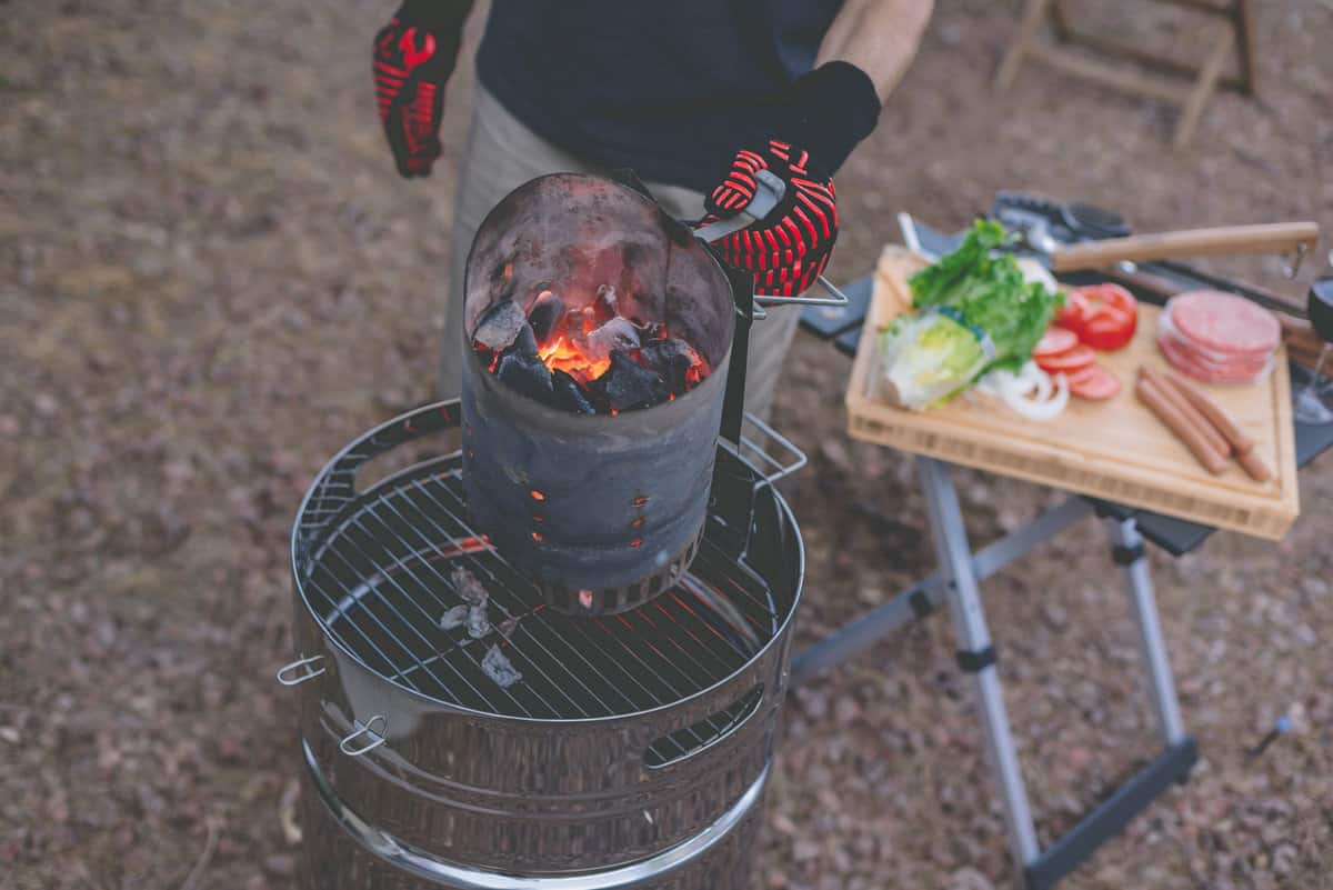 A man is starting his grill with a full charcoal chimney.