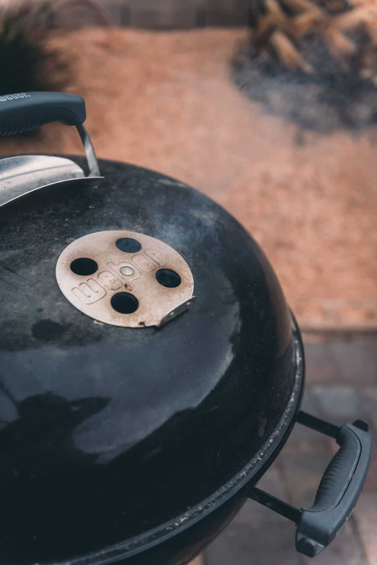 Weber grill with smoke coming out of the air vents. 