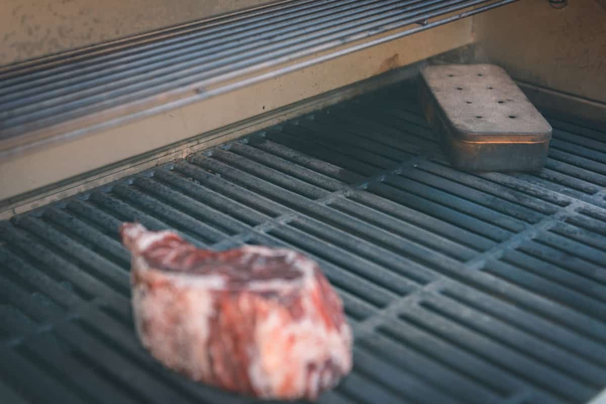 Smoket box on grill grates with a steak on the grill. 