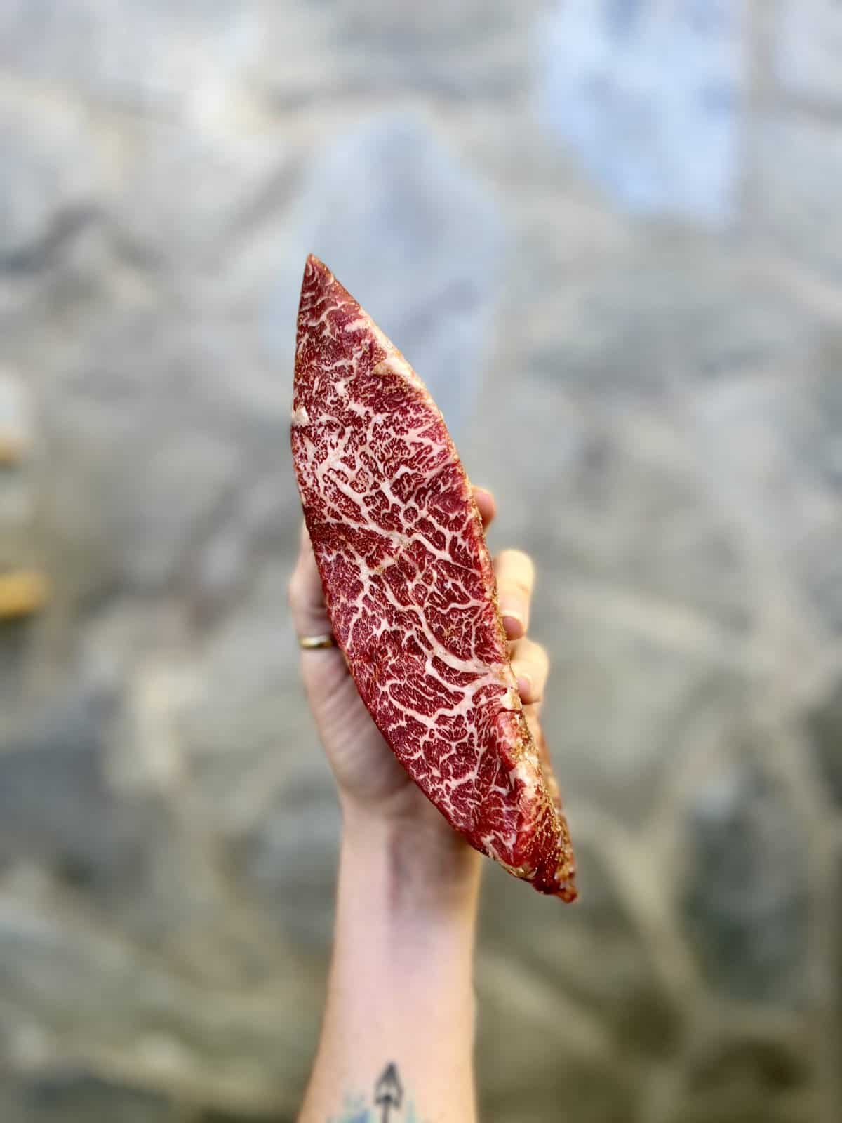 Hand holding a steak to show waygu marbling. 