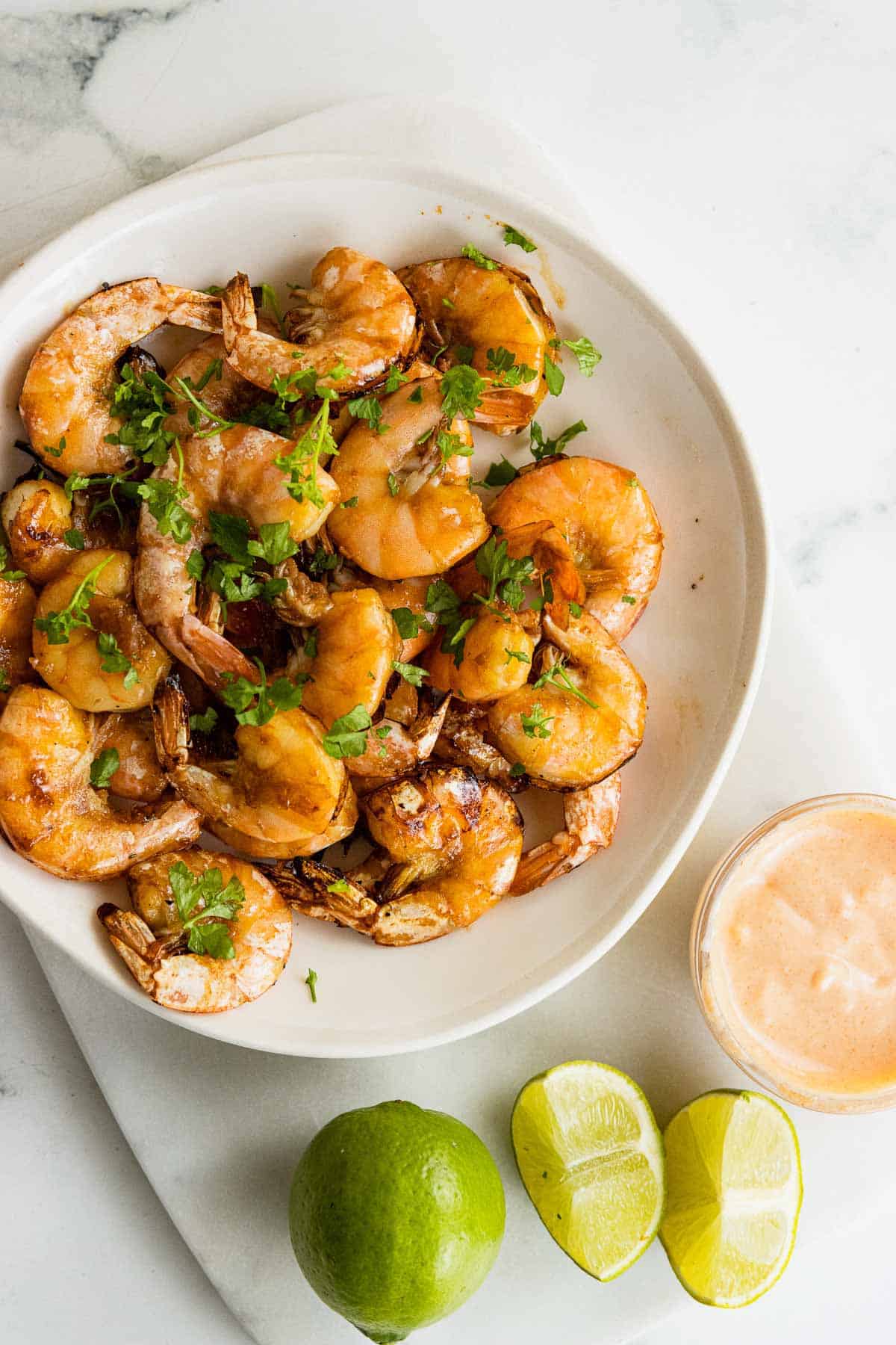 Overhead of bowl of soy honey air fryer shrimps with lime wedges.