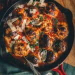 Close up of a spoon in a skillet of meatballs topped with cheese and marinara sauce.