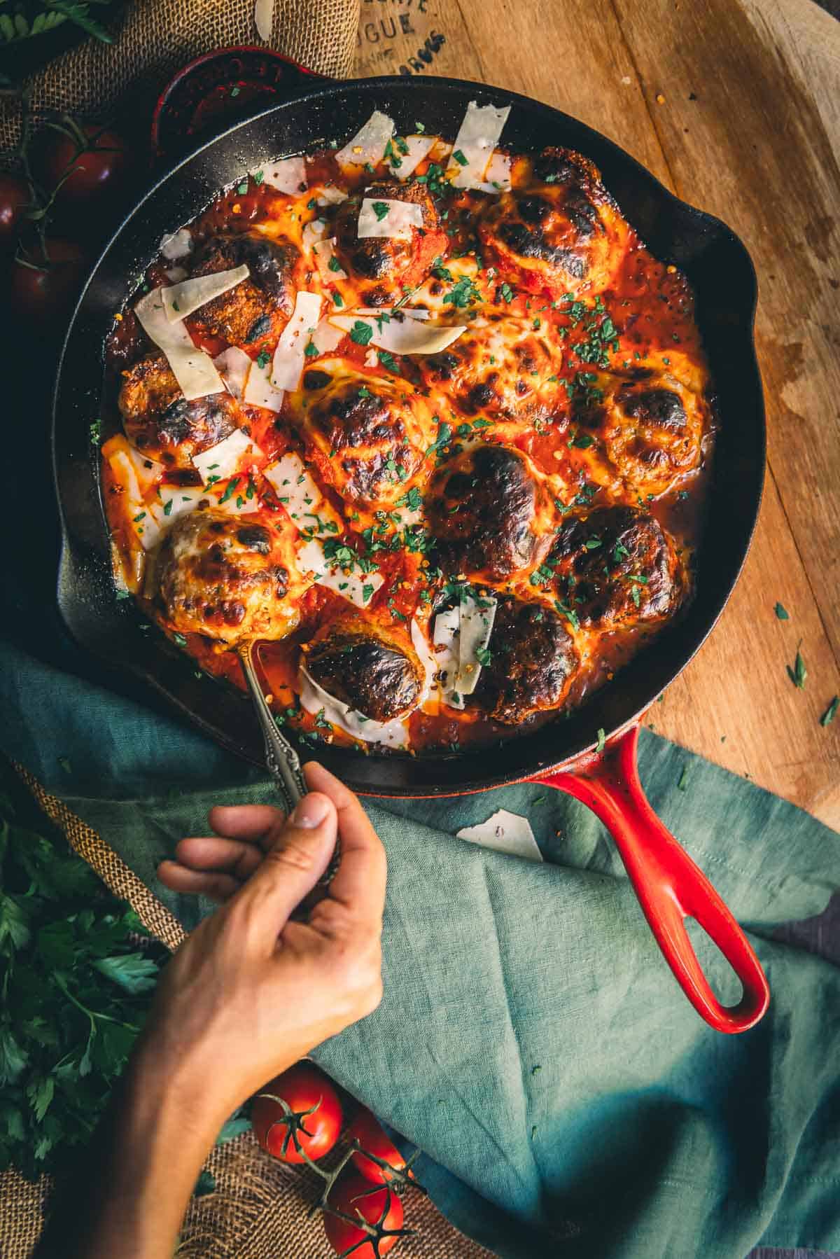 Hand spooning out a cheesy chicken meatball from a skillet. 