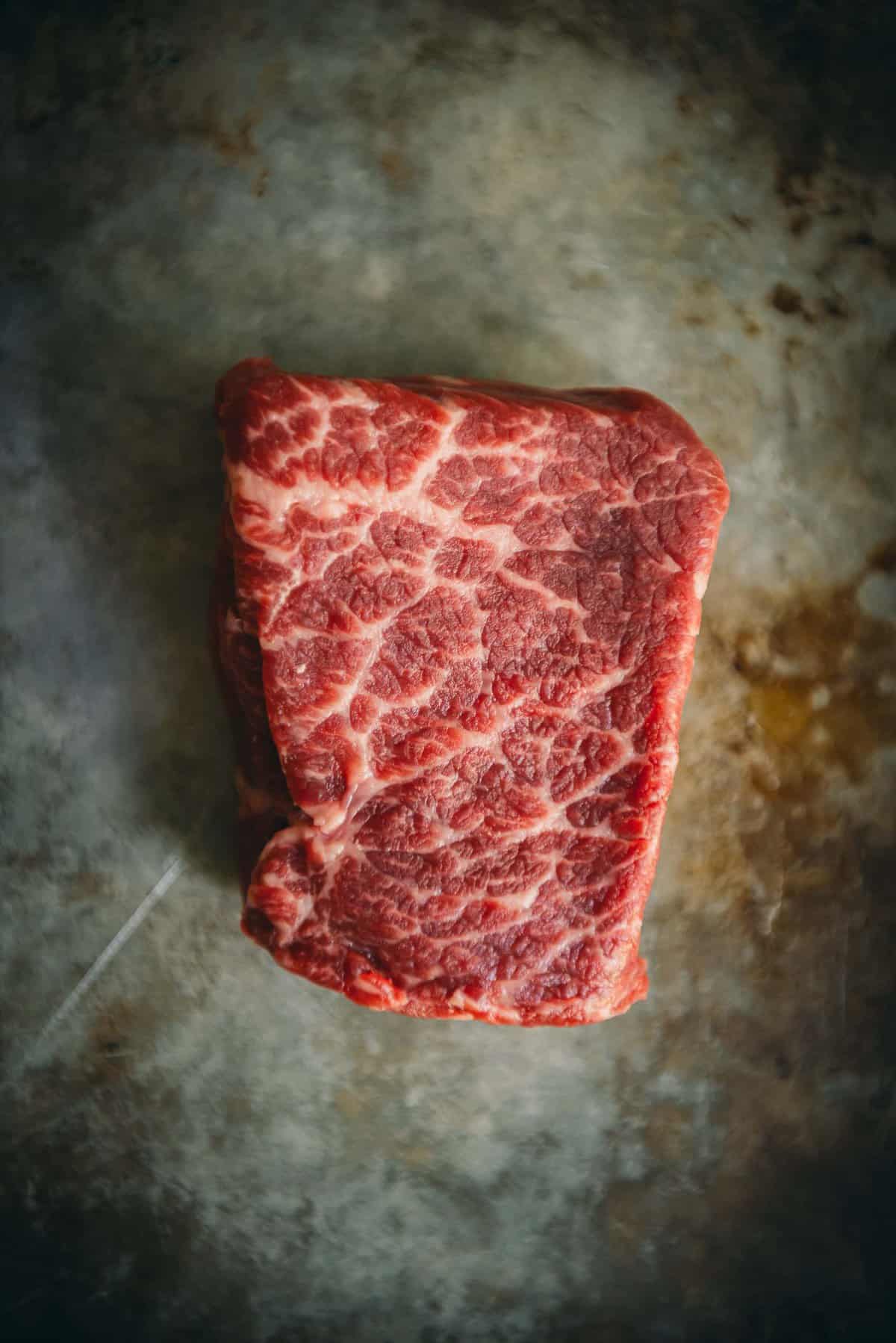 Raw petite denver steak showing white marbling running through the thick steak.