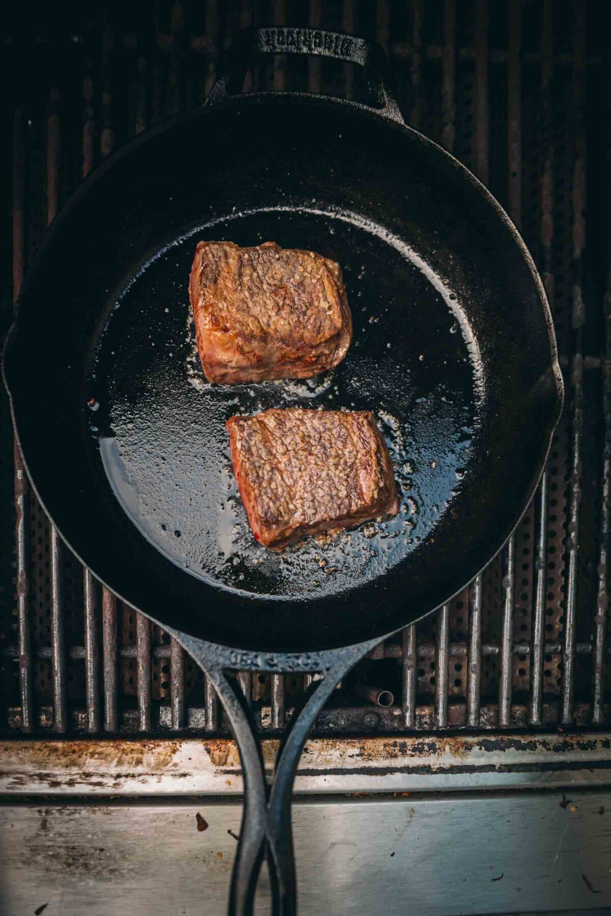 Steaks flipped in a skillet to show crust sitting on a grill. 