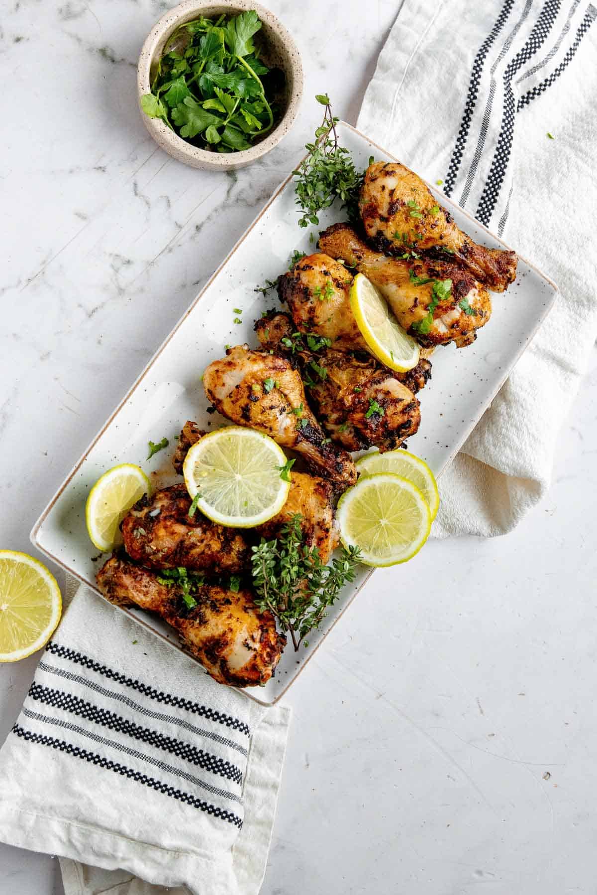 Chicken drums, cooked and lined up on a platter with lemon slices. 