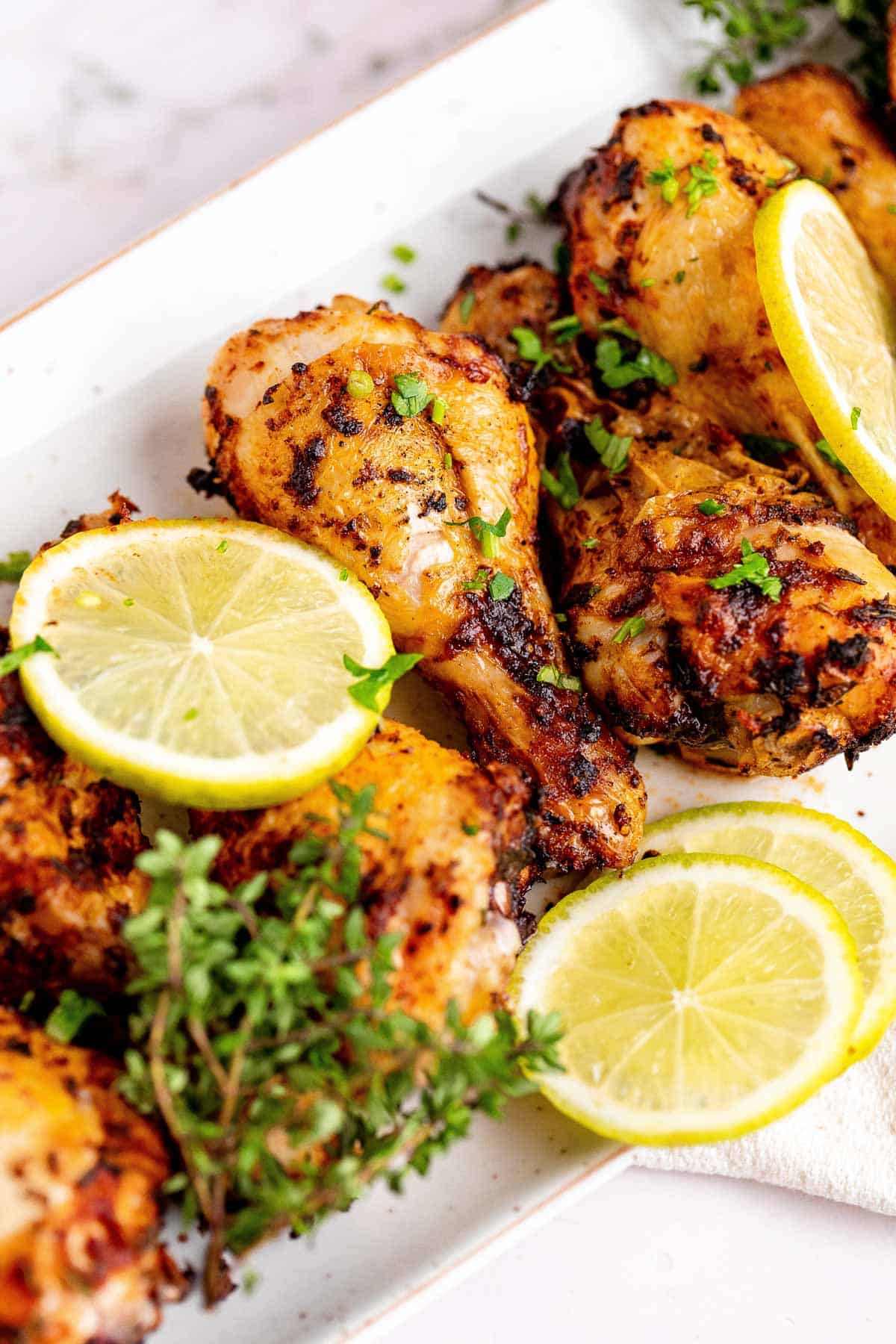 Chicken legs on a white platter with lemon slices and fresh herbs. 