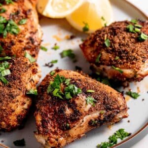 Chicken thighs on a white platter garnished with lemons and minced parsley.