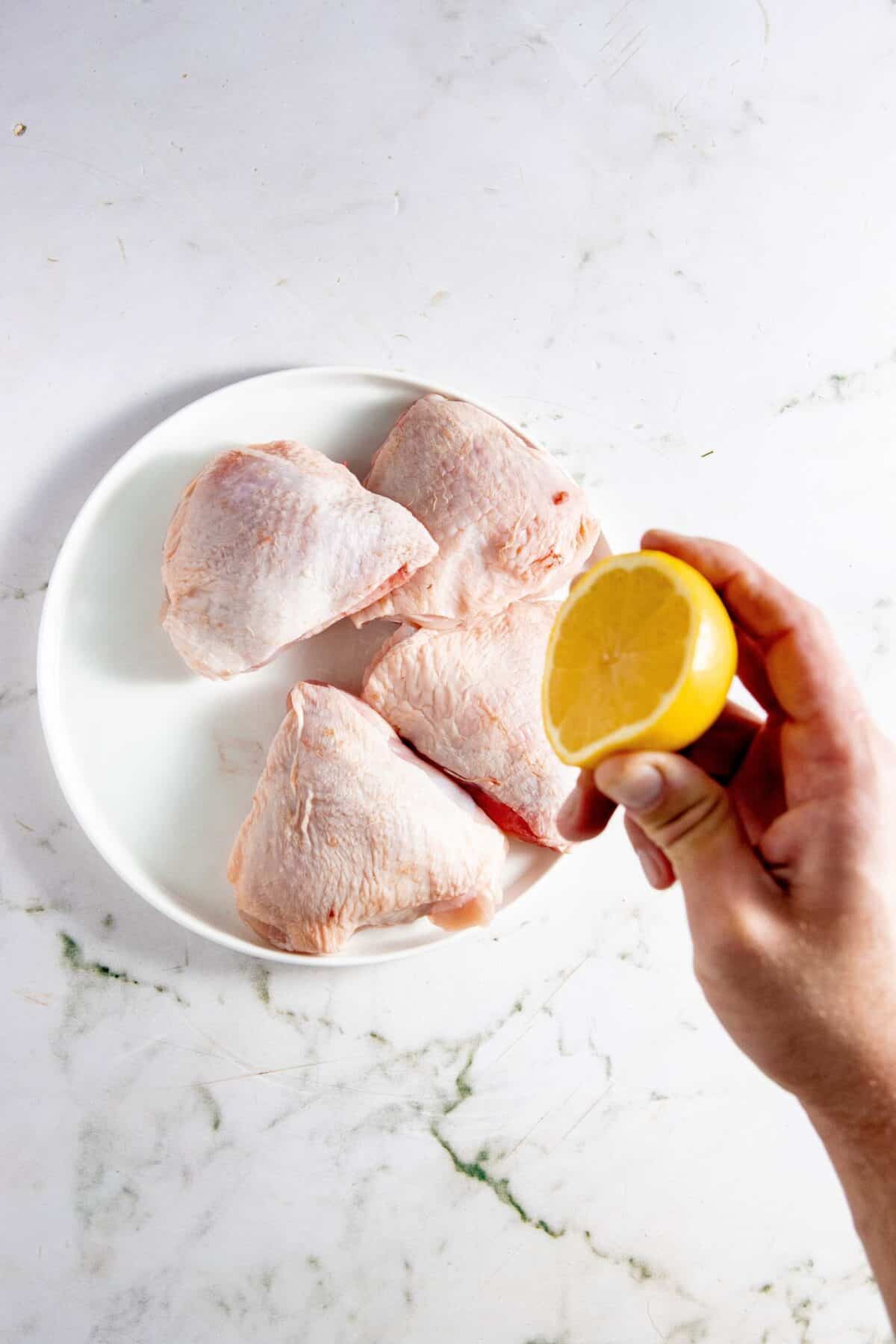 Hand squeezing lemon over chicken thighs.