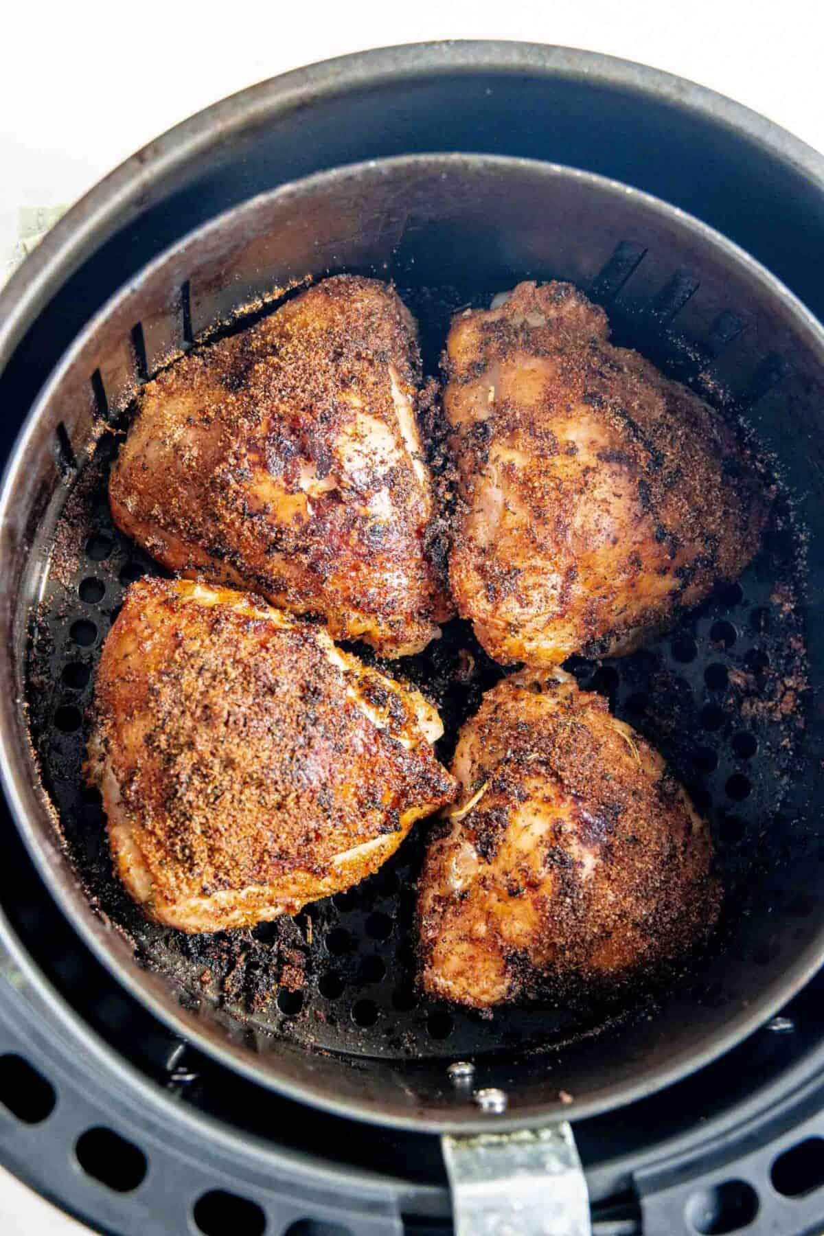 Spice rubbed chicken thighs in an air fryer basket.