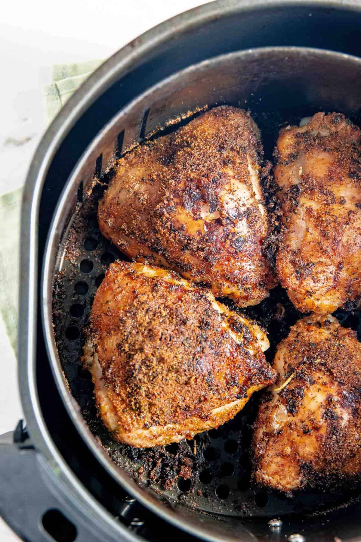 Golden brown spice rubbed chicken thighs in an air fryer basket. 