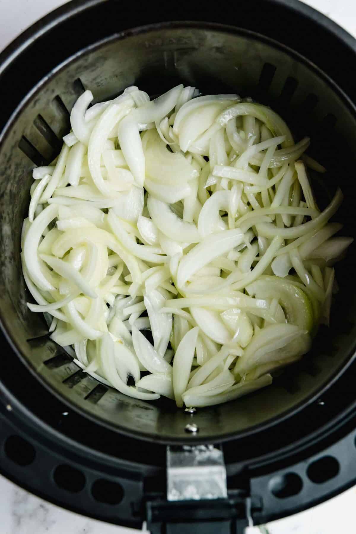 Raw onions in the basket of an air fryer.