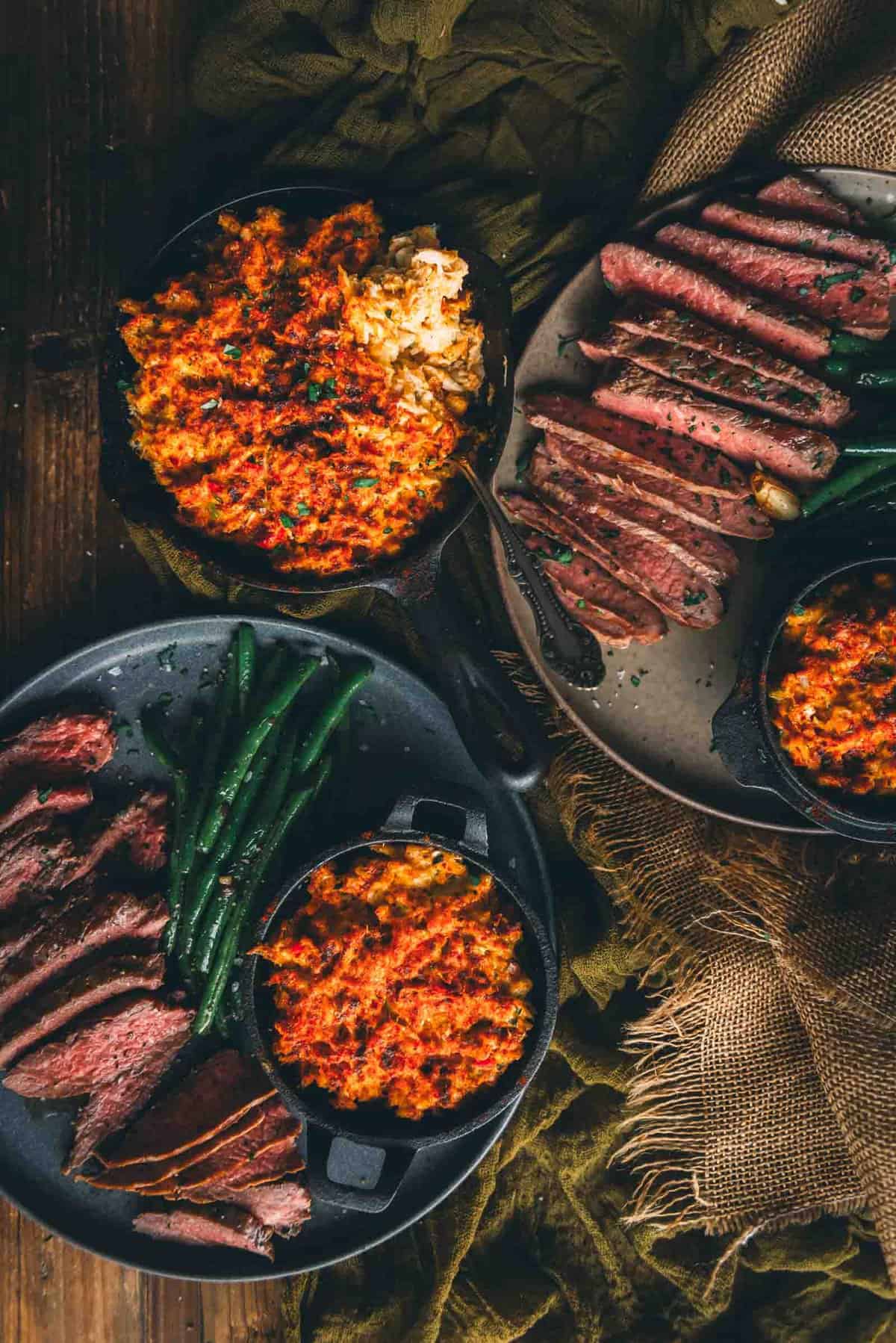 Table with plates of steak, green beans and crab in skillets.