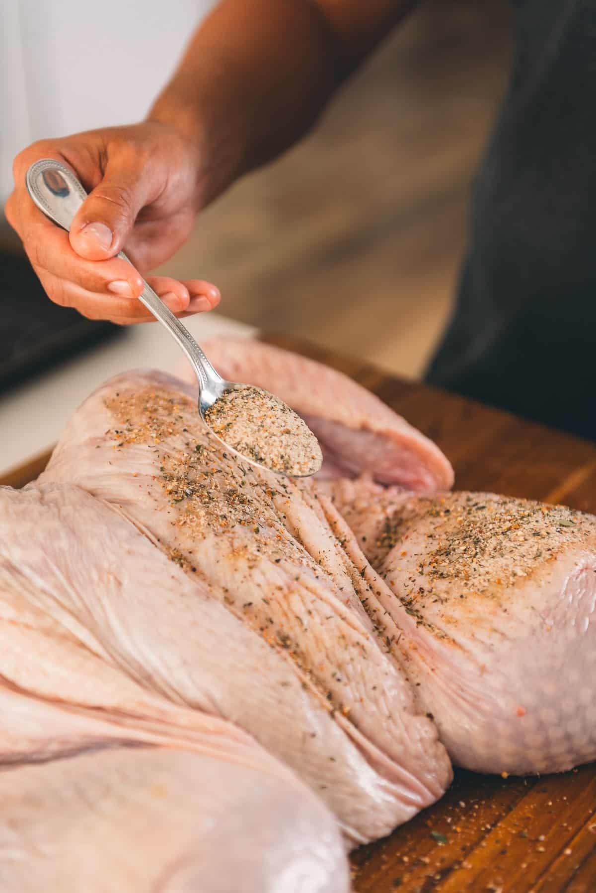 Hand holding spoon with salt mixture over turkey skin. 