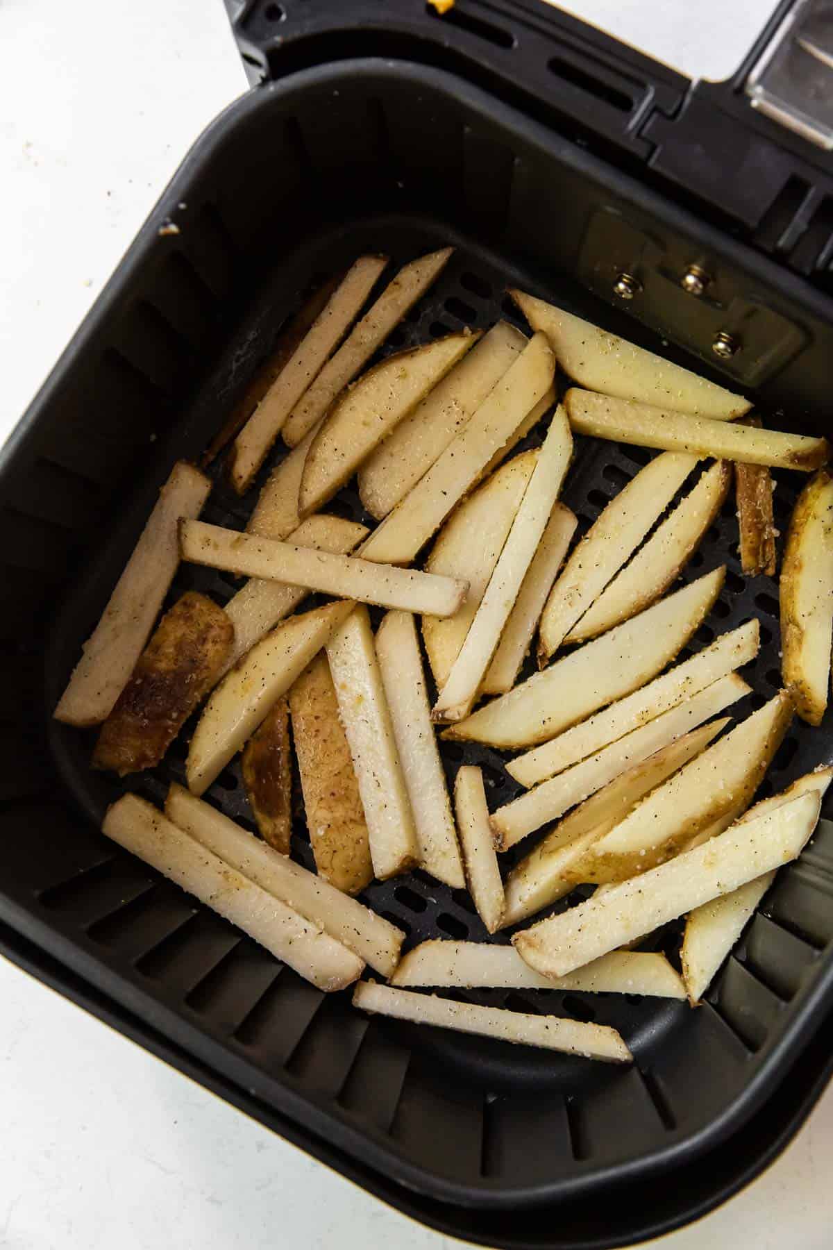 Seasoned sliced potatoes paced in the air fryer basket.