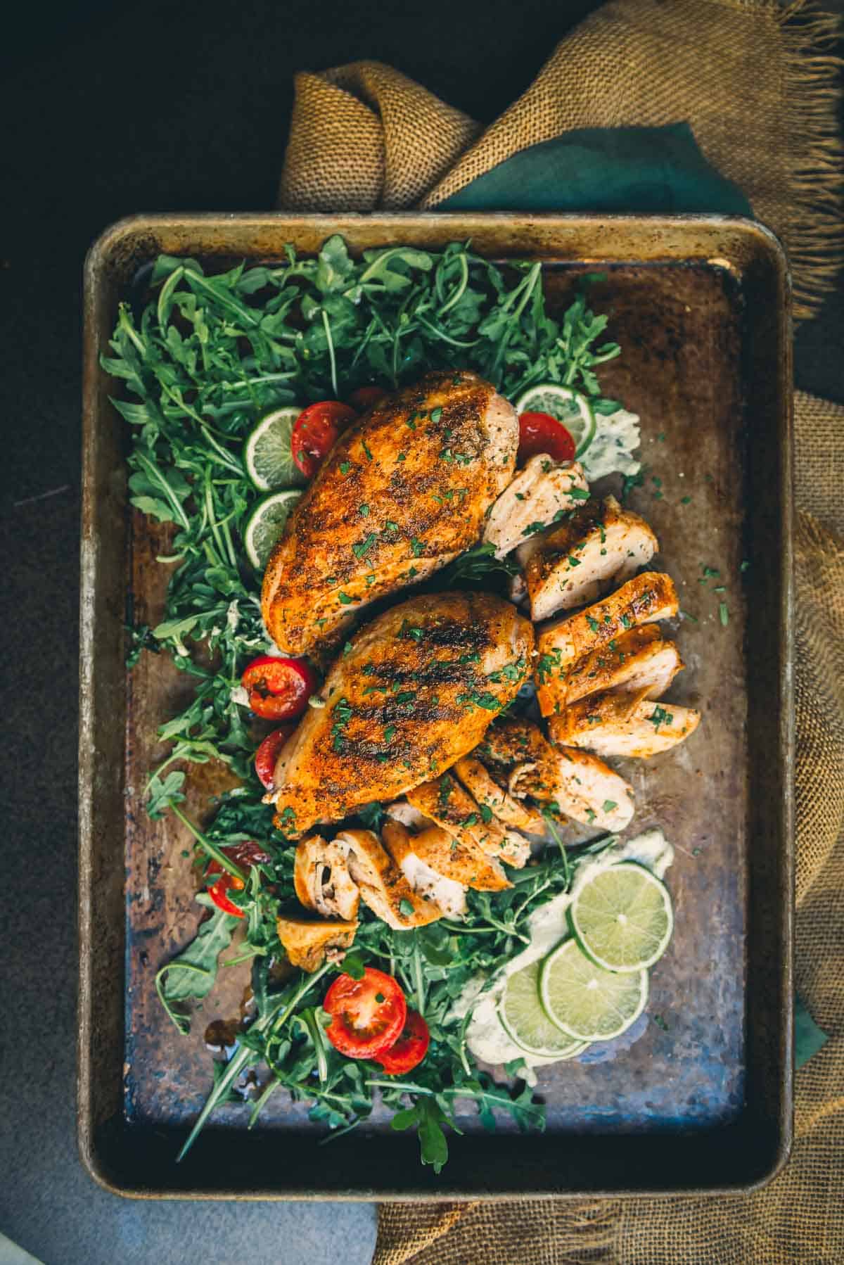 Grilled bone-in chicken on a platter with grill marks and one sliced for serving.