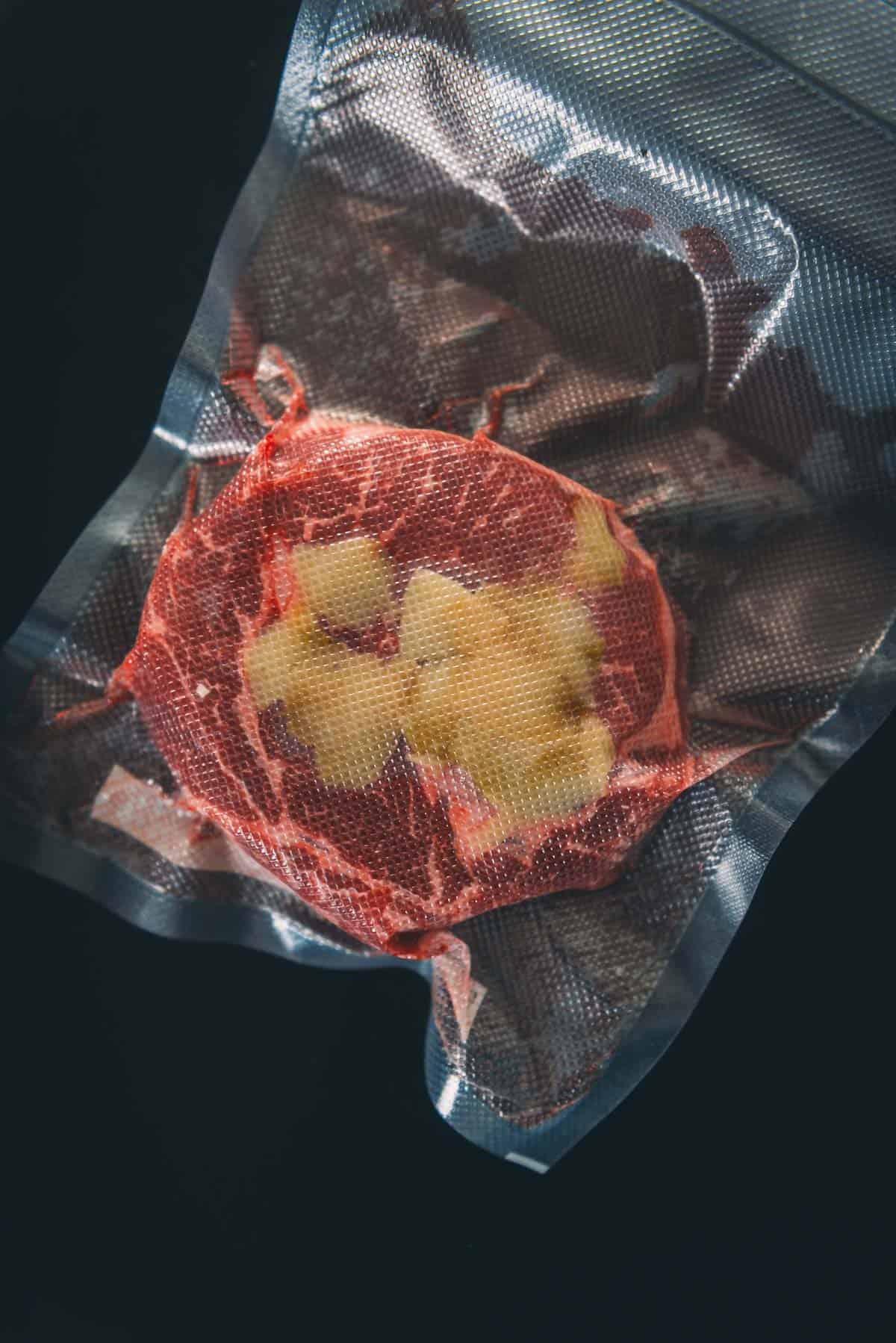 A steak in a vacuum sealed bag with garlic.
