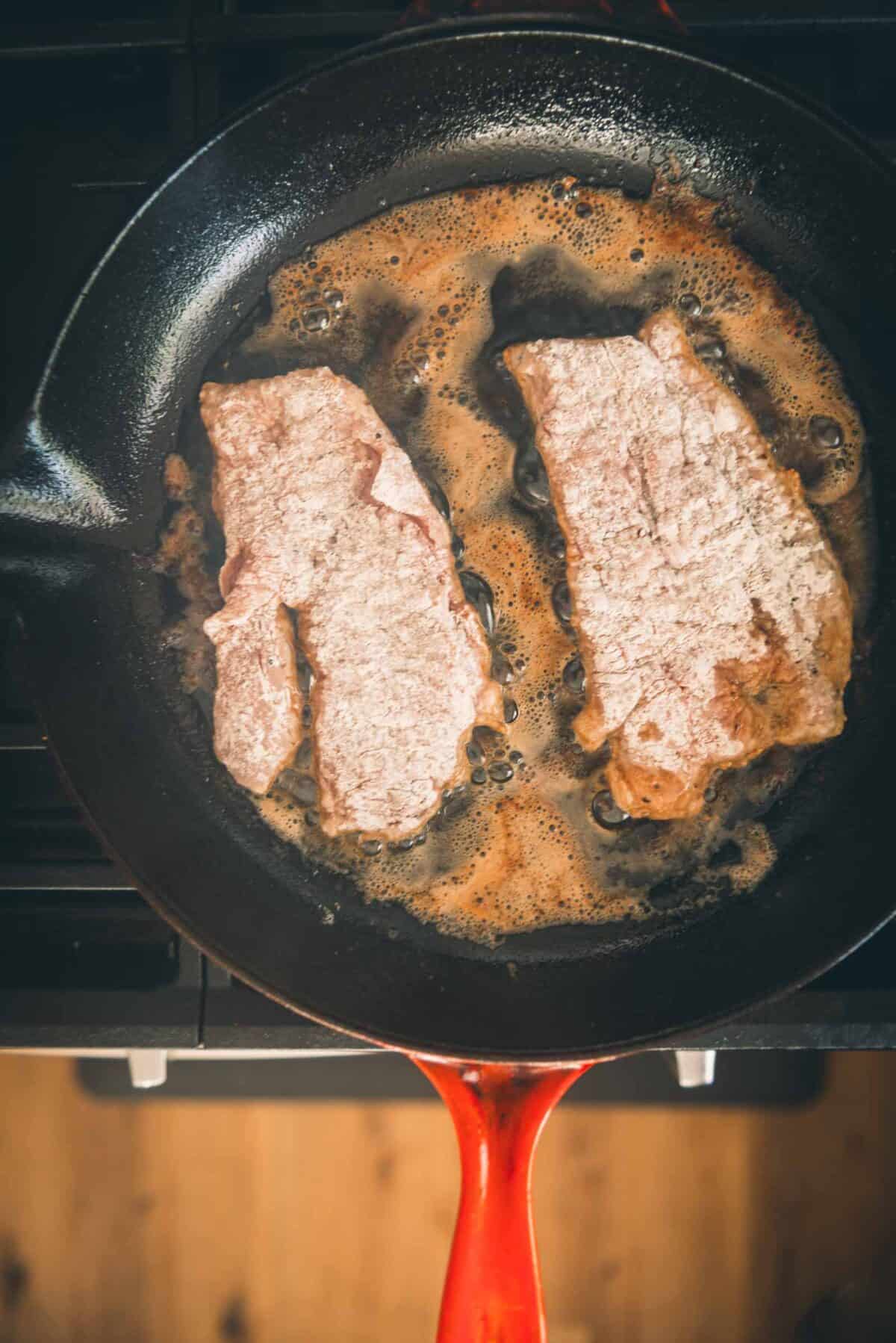 Veal cutlets in a frying pan on top of a stove.