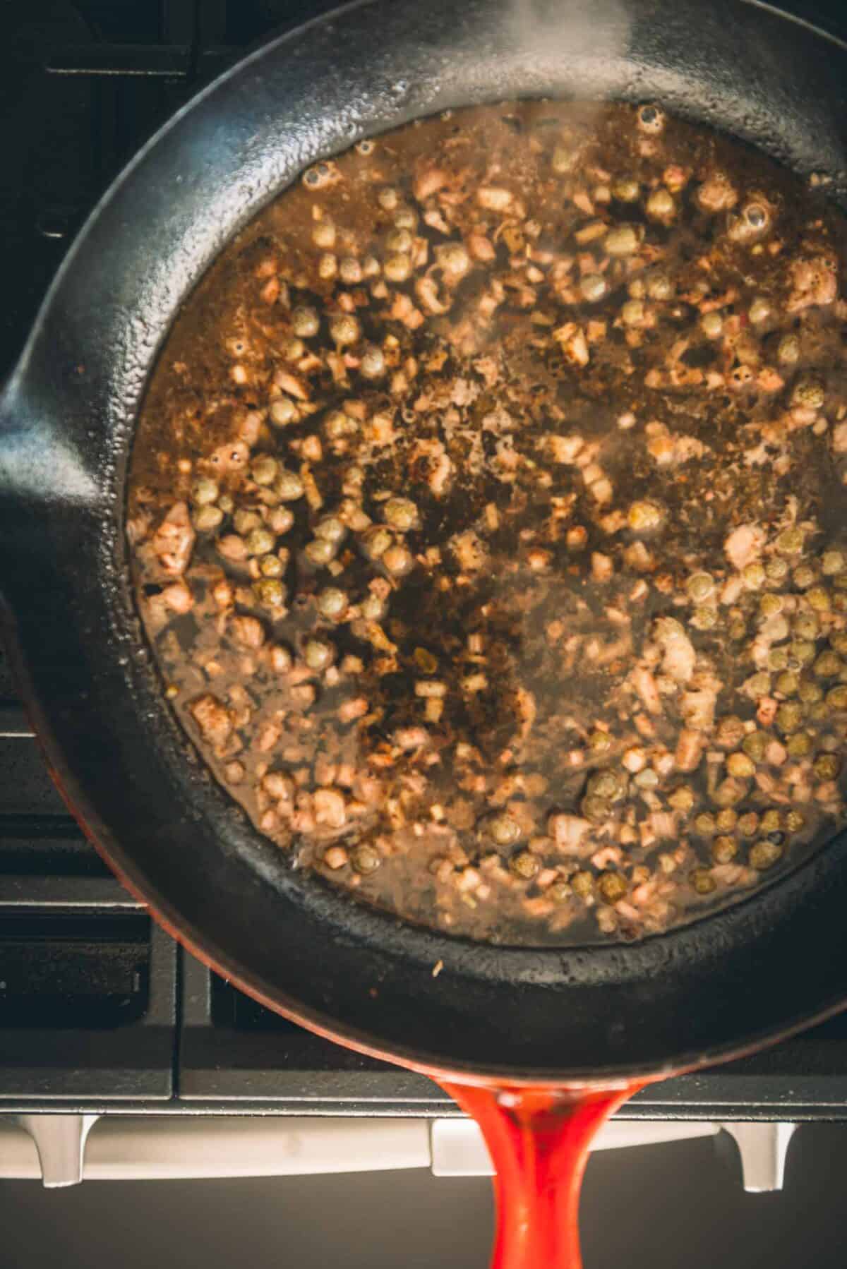 A frying pan filled with shallots and peas.