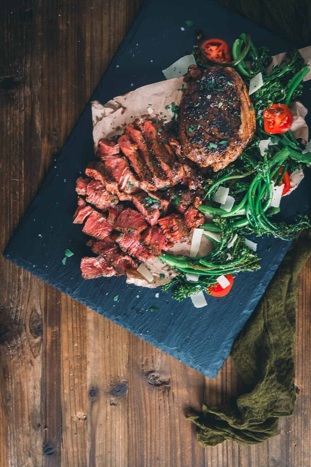 Sliced steak on a serving board on a wooden table.