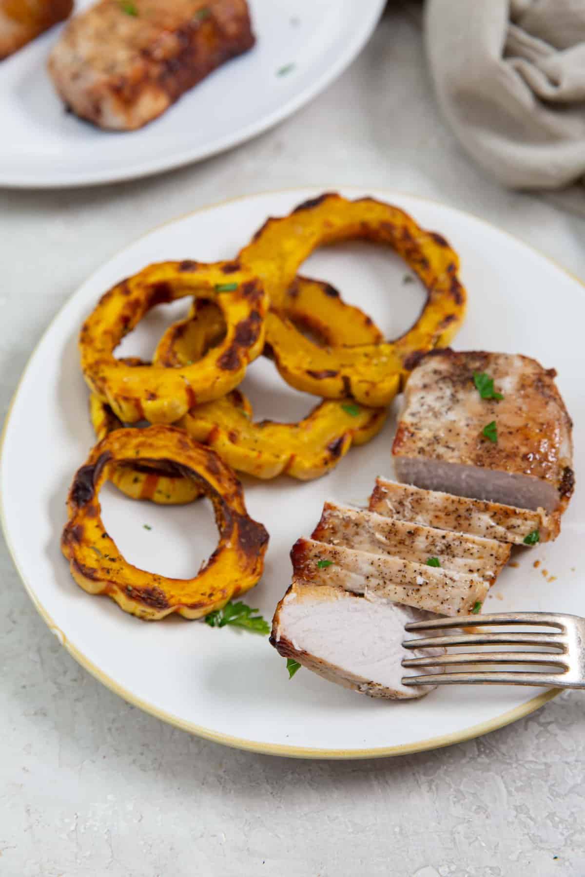 Sliced thick pork chop on a white plate with squash rounds.