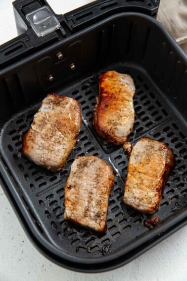 Thick pork chops browning in an air fryer.