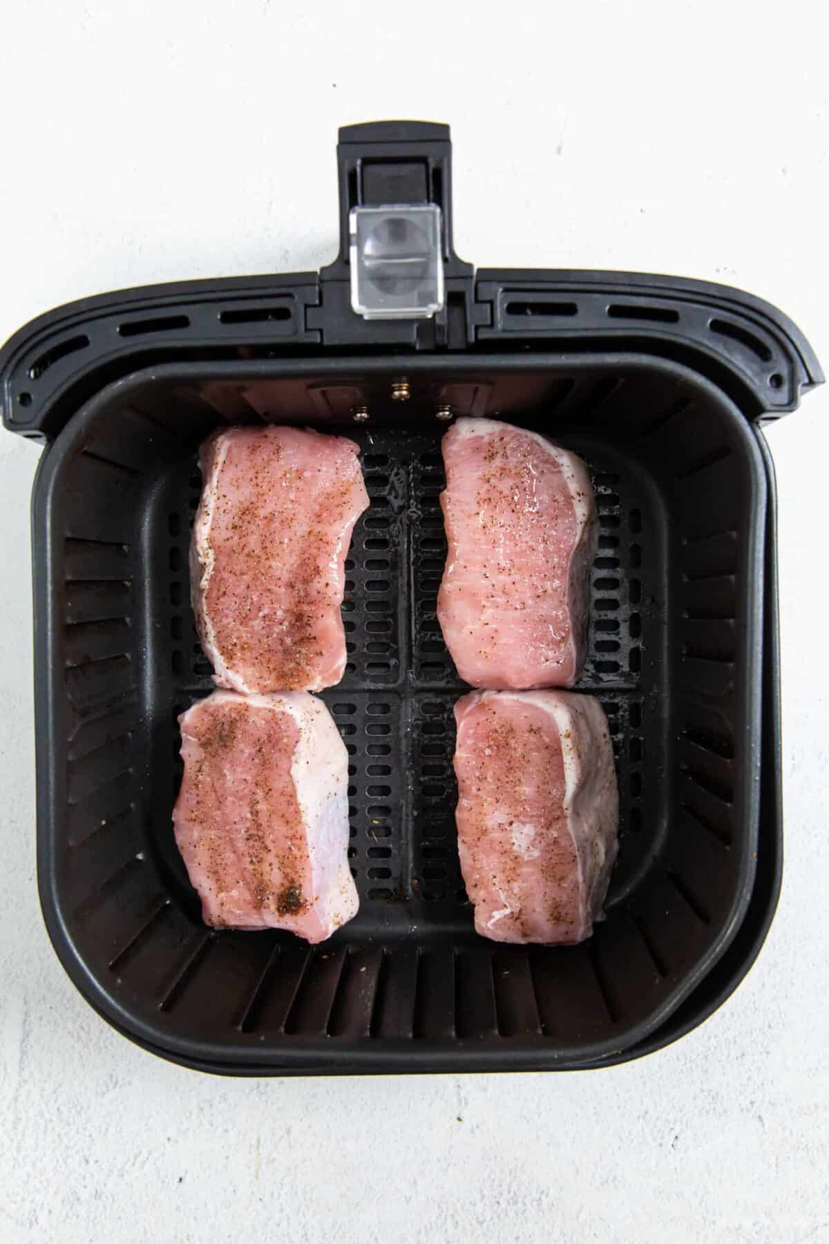 Seasoned pork chops placed in the air fryer in a single layer.