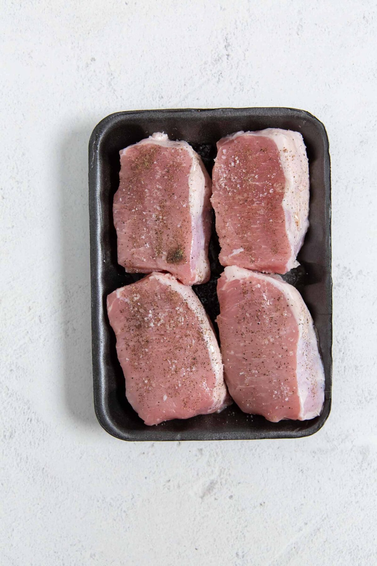 Raw pork chops seasoned with salt and pepper.